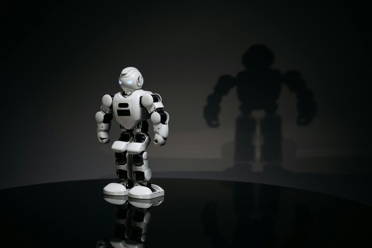 A white and black toy humanoid robot in a studio setting casting a shadow.